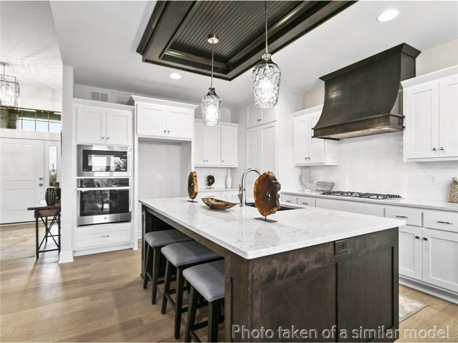 Kitchen with recessed lighting, a tray ceiling, stainless steel appliances, a center island with sink, and premium range hood